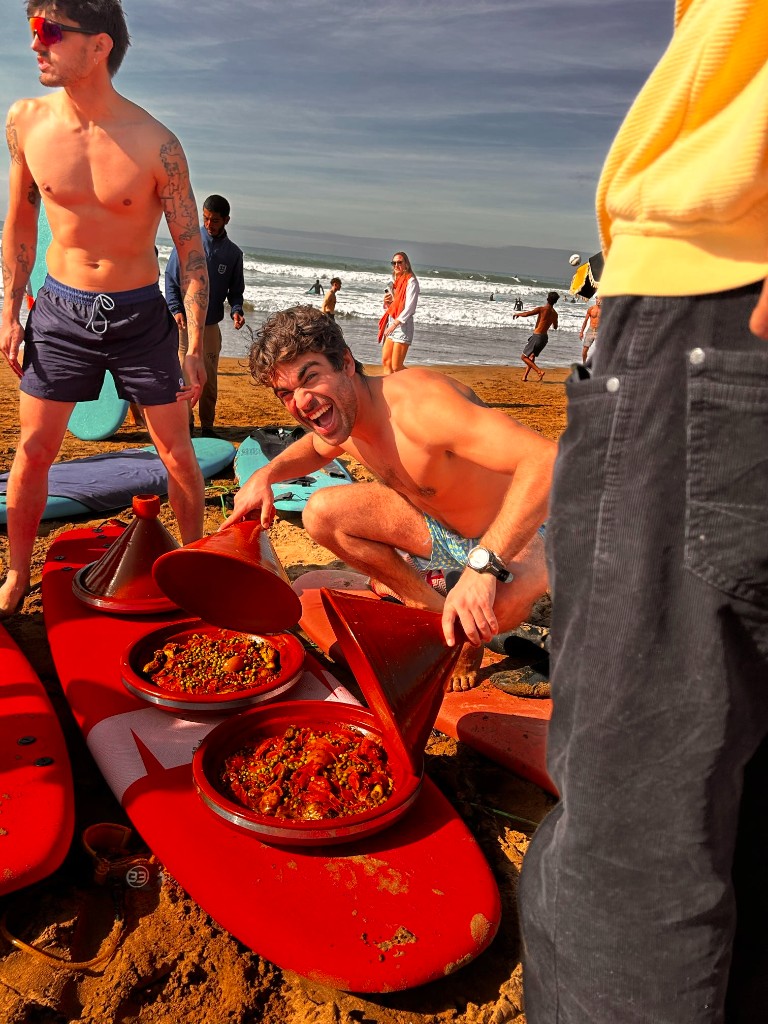 Friends sharing tajine on the beach with surfboards in Tamraght